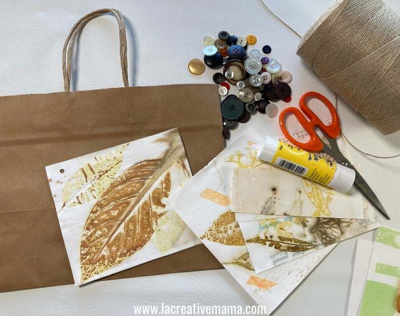 a brown paper bag, a variety of eco prints on paper, glue, scissors and old buttons