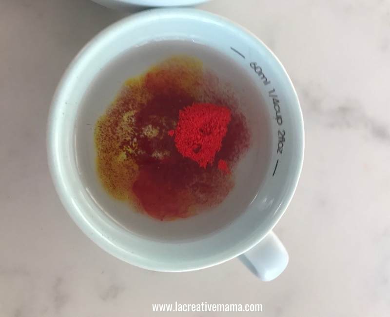 dissolving red food coloring in  cup of water