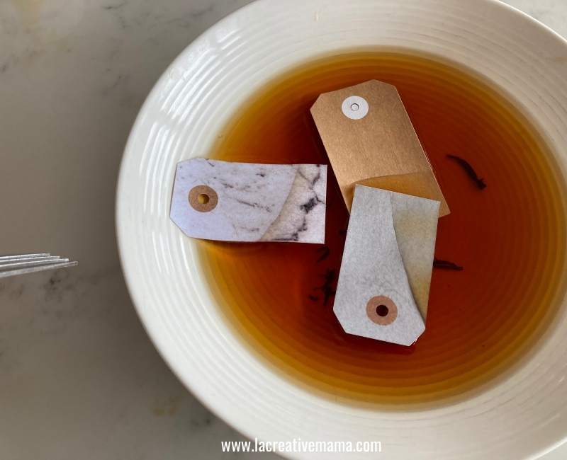 3 paper gift tags immersed in a tea bath 