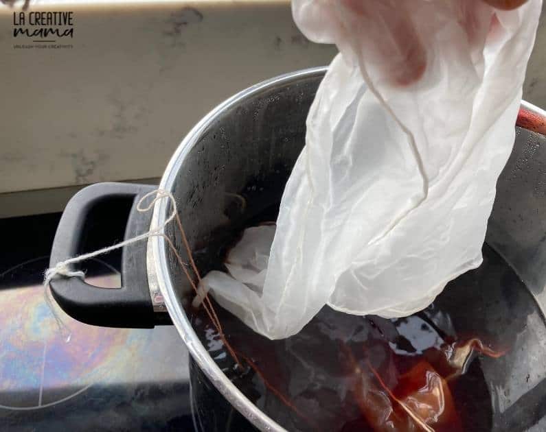 immersing a white silk fabric inside a dye pot filled with logwood dye solution 