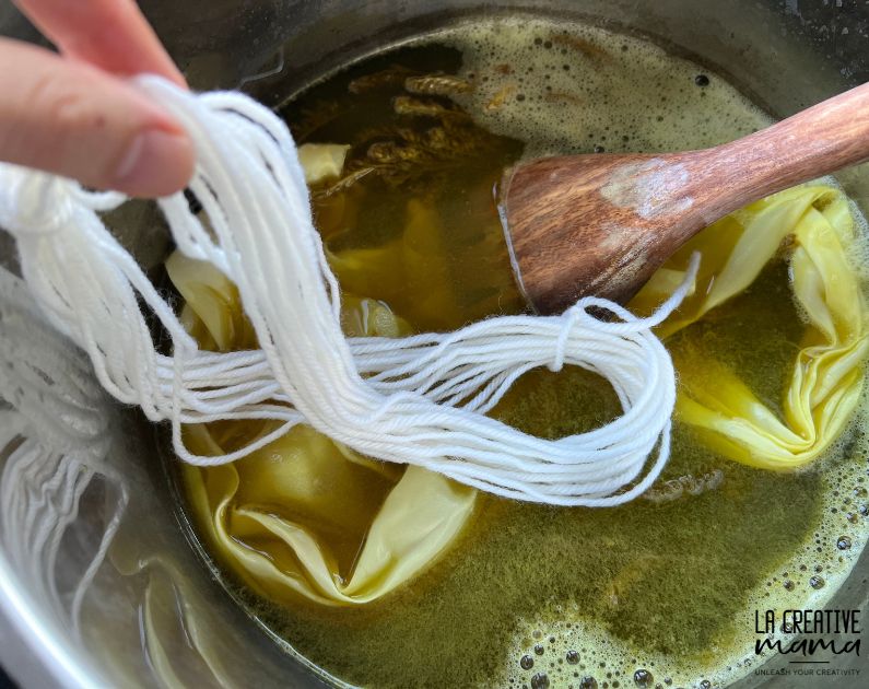 immersing white wool yarn inside a pot that has goldenrod dye liquid. 